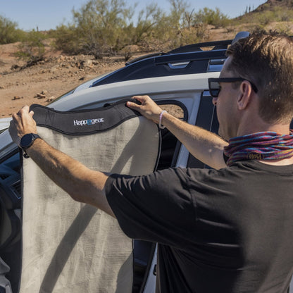 Man in sunglasses draping a sand-colored Happeseat car seat cover over a white SUV seat in a desert setting